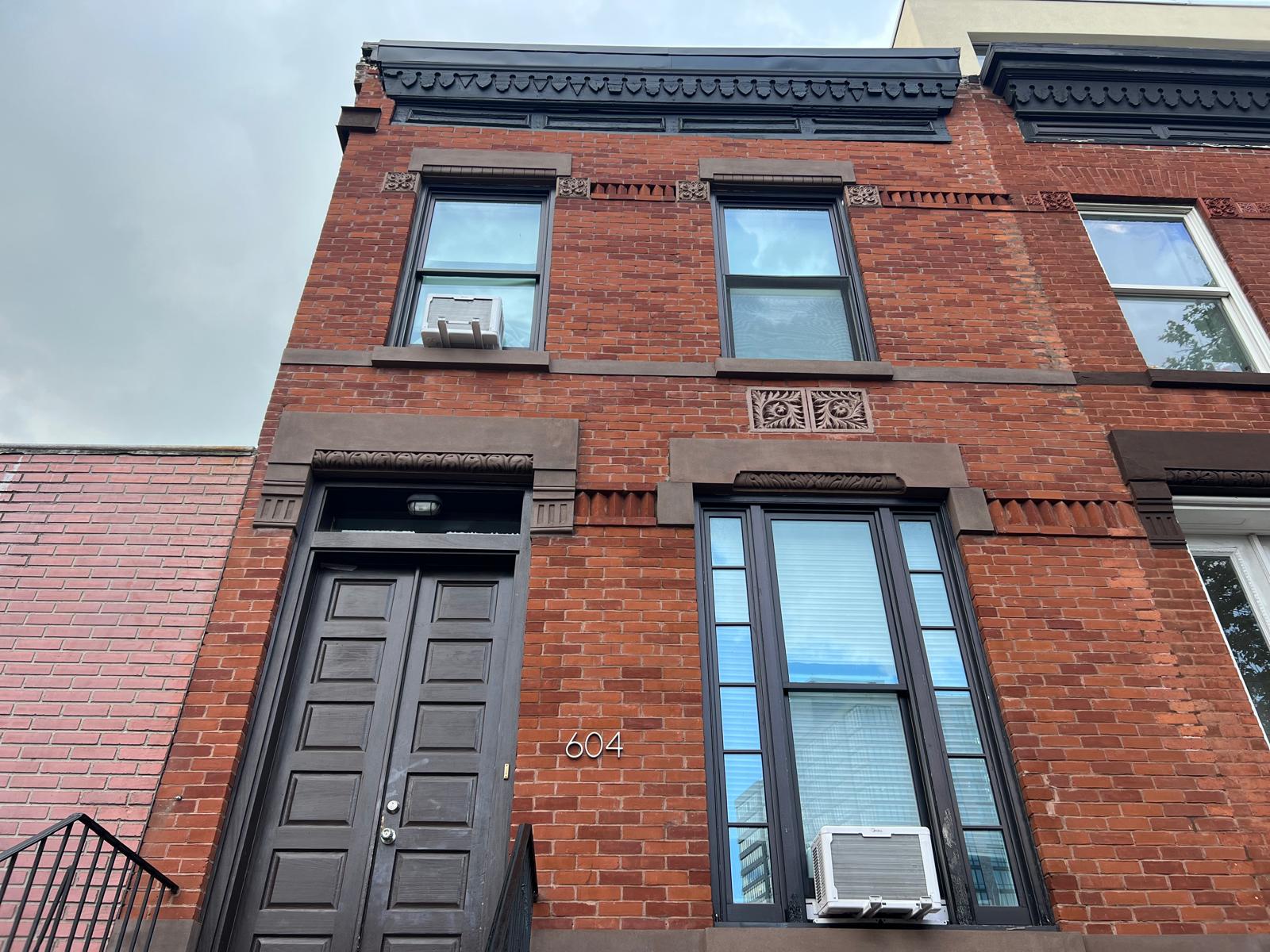 Restored Italianate cornice with hand-carved brackets, brownstone window hoods, and ornamental floral medallion on a Brooklyn brick rowhouse façade